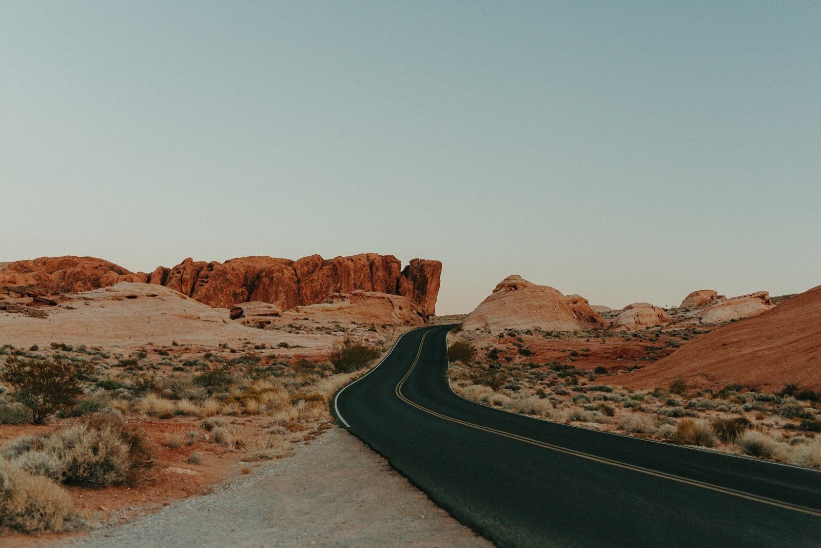 A winding road cuts through red sandstone hills and desert scrub under a clear sky on the Phoenix-to-Los Angeles drive.