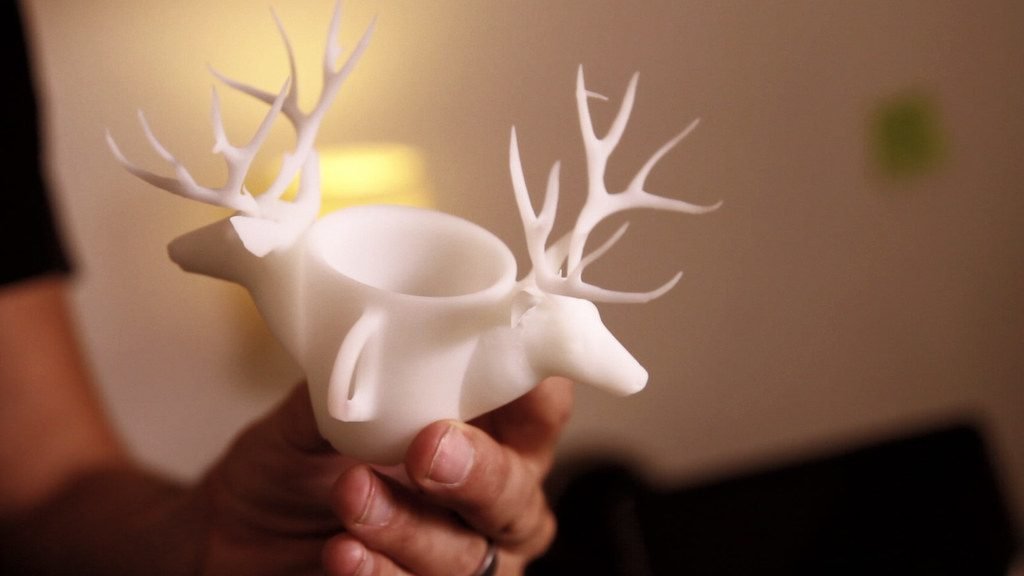 A hand holds a white 3D printed deer cup with large antlers and a hollow top, matching the creative printer project theme.